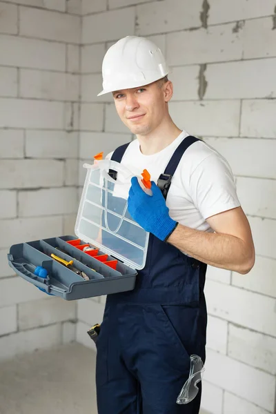 Bonito trabalhador da construção masculina com uma caixa de ferramentas isolada contra uma parede de tijolo — Fotografia de Stock