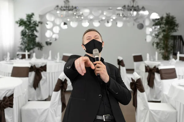 在rastoran的宴会厅里，身穿西服，戴着防护面具，手里拿着话筒的人 — 图库照片