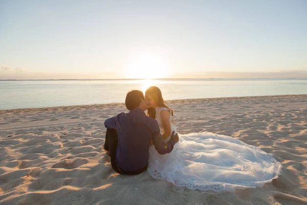 Menyasszony és vőlegény ülnek a homokon. — Stock Fotó