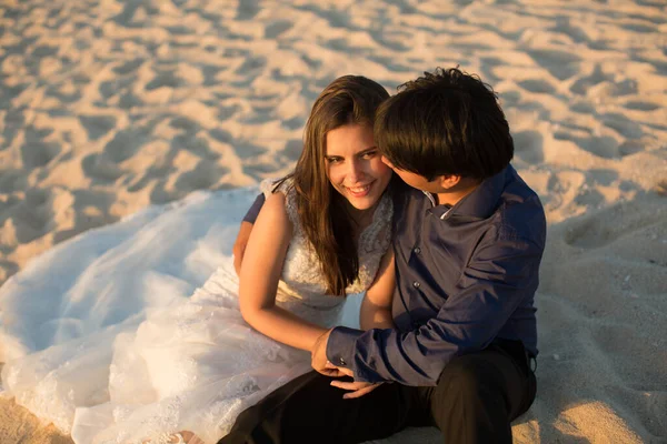 Bride and groom sit on the sand. — Stock Photo, Image