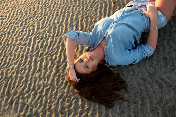Ung flicka liggande på sanden vid solnedgången. — Stockfoto