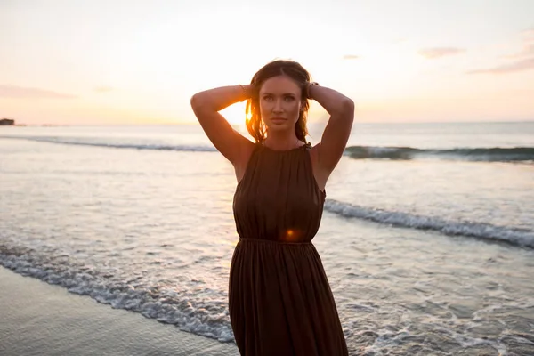 Mooie vrouw op zonsondergang achtergrond. Kleurrijke dageraad boven de zee. Zorgeloze vrouw die geniet van de zonsondergang op het strand. Gelukkige levensstijl. — Stockfoto