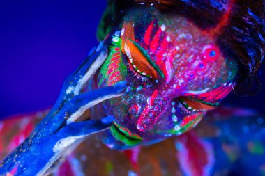 Vücut sanatı ultraviyole ışıkta parlıyor. Ultraviyole ışıkta parlayan bir kızın vücudunda ve elinde vücut sanatı.