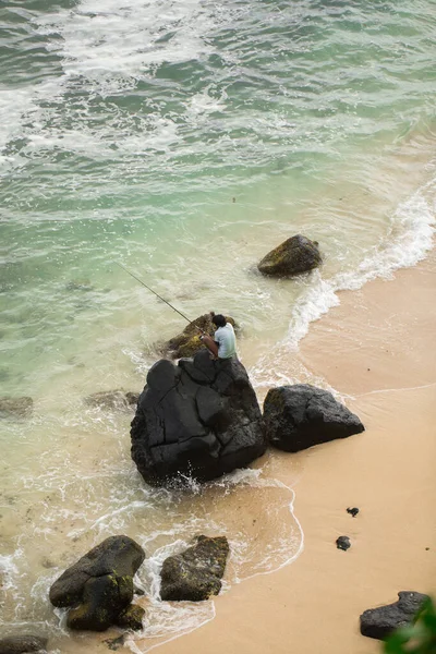 Rybář rybaří v černých kamenech v oceánu — Stock fotografie