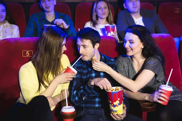 Duas raparigas e um tipo a ver uma comédia num cinema. Jovens amigos assistindo filme no cinema. Grupo de pessoas no teatro com pipocas e bebidas . — Fotografia de Stock