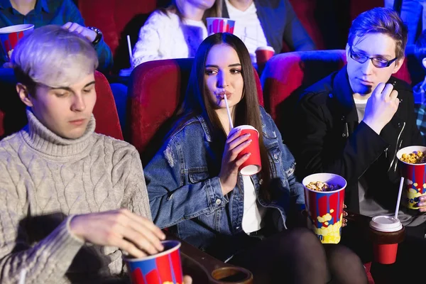 Vrolijk gezelschap in de bioscoop. Een meisje drinkt uit een glas, een man eet popcorn. — Stockfoto