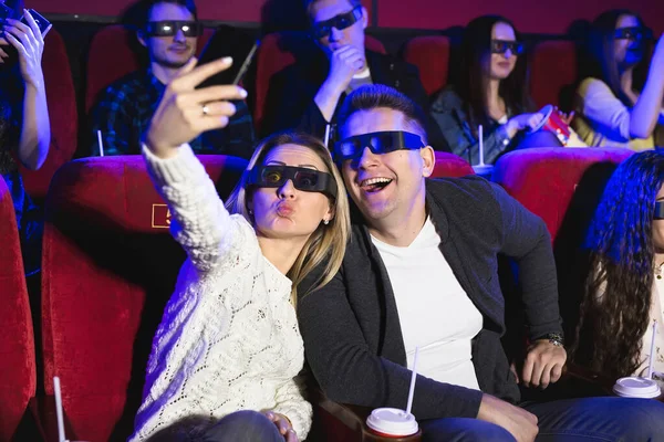 Mooi meisje en man lachen gelukkig samen een selfie te maken tijdens een film in de bioscoop. Mooi en positief meisje en jongen zijn het nemen van selfie. — Stockfoto