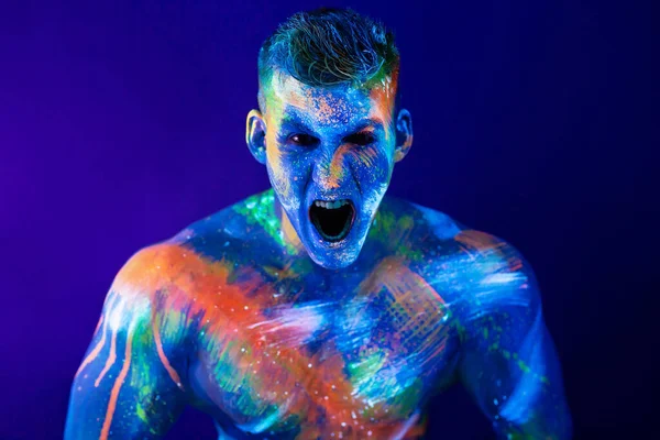 Grita un joven. Pintura fluorescente en cara y torso muscular, en plano de estudio con luz UV. — Foto de Stock