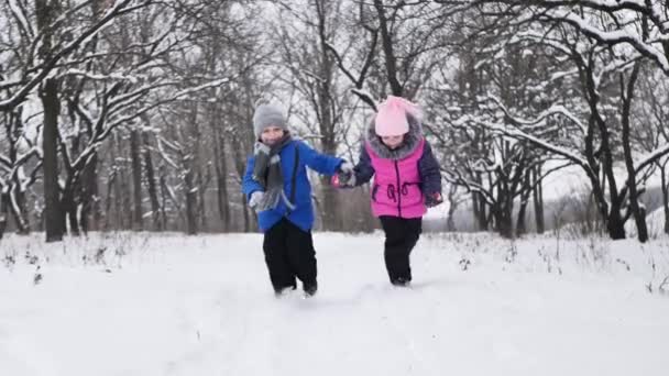 Bambini, un ragazzo e una ragazza si tengono per mano e corrono in inverno nella foresta. Rallentatore. — Video Stock