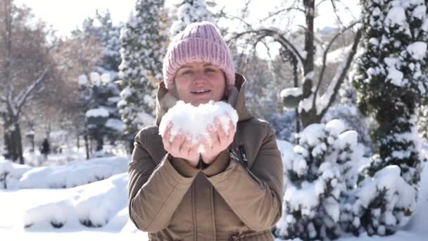 Soğuk havada karı uçuran bir kadın. Ellerinde kardan bir kalp. Kar taneleri uçuşuyor — Stok video