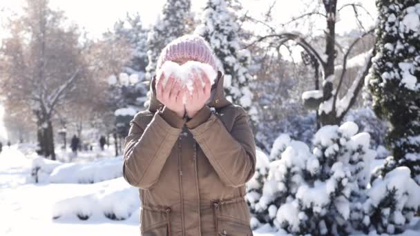 Mulher sopra neve no tempo gelado. Um coração de neve nas tuas mãos. Flocos de neve estão voando — Vídeo de Stock