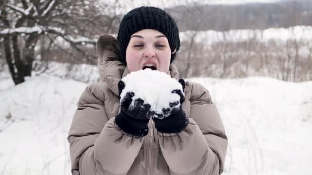 年轻的漂亮姑娘第一次在雪地上从她的手中吹到相机前。B.冬季森林的背景 — 图库视频影像