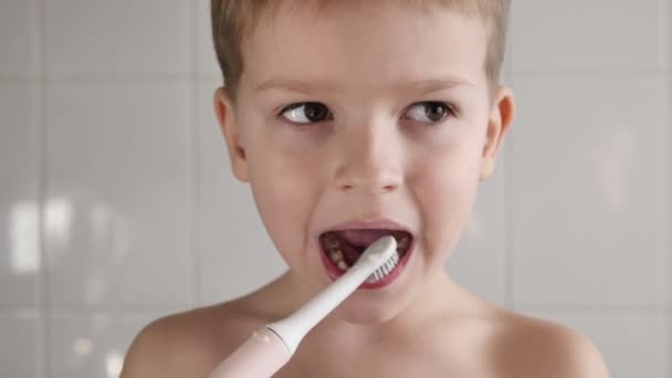 Portret van een leuke jongen poetsen zijn tanden met een elektrische borstel in de badkamer — Stockvideo