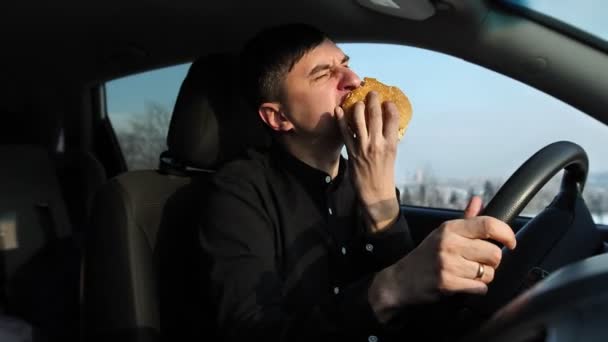 Mężczyzna jadący samochód podczas jedzenia hamburgera. Oczekiwania i stojąc w korku — Wideo stockowe