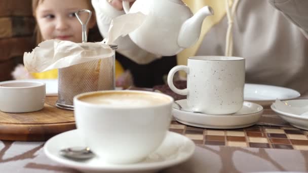 Vacaciones familiares en un café. Mamá vierte té de una tetera en una taza — Vídeos de Stock