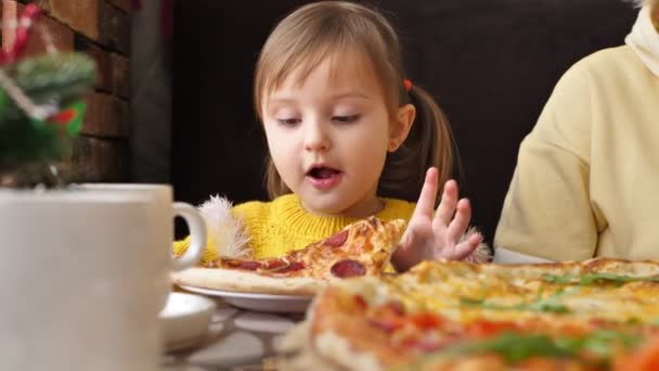 Little cheerful girl bites pizza in a cafe and gives a thumbs up, like — Stock Video