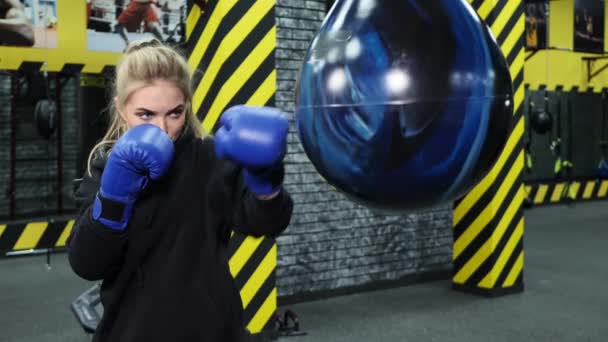 Молода жінка-спортсменка в блакитних боксерських рукавичках потрапляє в грушу . — стокове відео