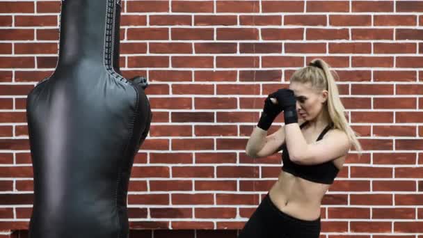 Mujer joven entrena en el ring de boxeo con saco de boxeo pesado. Patadas en los pies o golpe de rodilla — Vídeo de stock