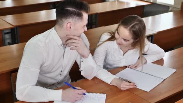 Studenter: en kille och en tjej i klassrummet vid skrivbordet tittar på varandra, skrattar och håller varandra i handen — Stockvideo