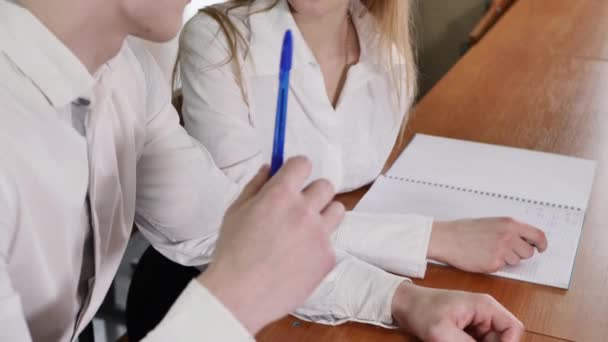 Estudiantes: un chico y una chica en el aula en el escritorio se miran y sonríen — Vídeos de Stock