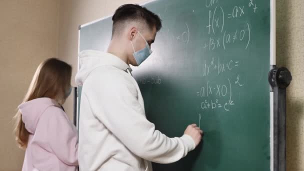 Група студентів з маскою обличчя, які пишуть на дошці в класі під час пандемії . — стокове відео