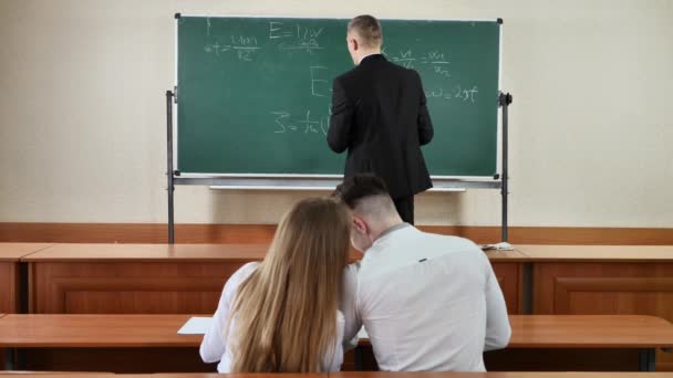 Lärare ger en föreläsning i ett klassrum och skriva matematiska formler i styrelsen. — Stockvideo