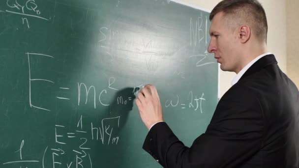 Educação, aprendizagem, matemática e o conceito de pessoas. A mão de um professor do sexo masculino escreve uma equação matemática no quadro negro — Vídeo de Stock