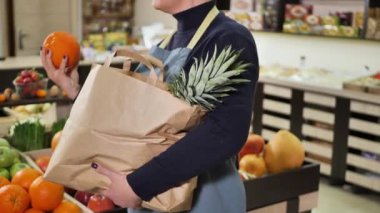 Genç pazarlamacı, kese kağıdında sebze ve meyve topluyor.