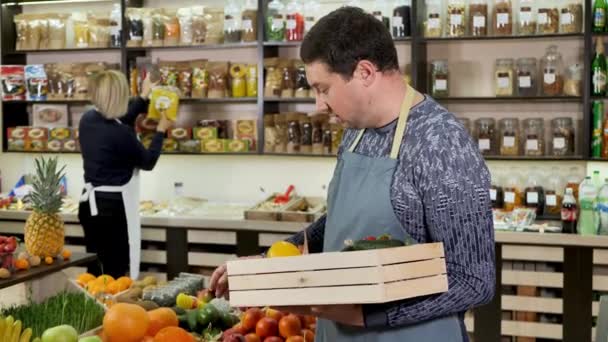 Male store clerk puts vegetables and fruits in a wooden box — Stock Video