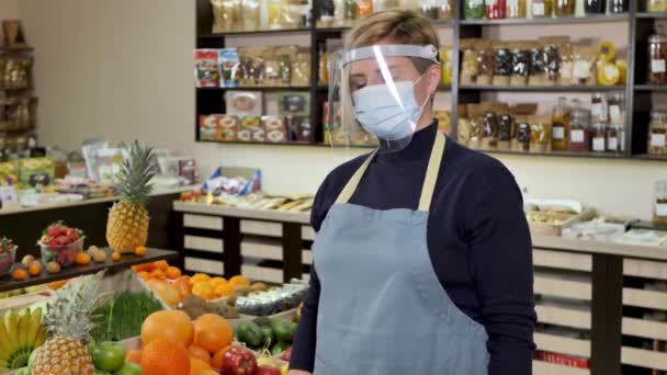 Close-up portrait of a happy, smiling female grocery store worker wearing a protective mask and gloves, holding a pineapple. — Stock Video