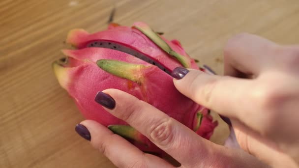 Nahaufnahme von Händen, die mit einem schwarzen Messer auf einem Holzbrett eine Pitahaya-Frucht schneiden — Stockvideo