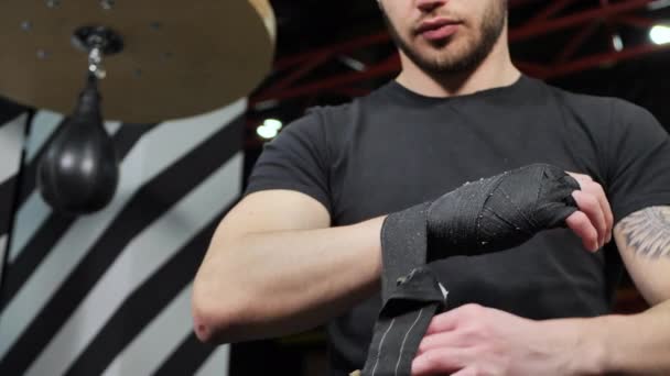 Чоловік обмотує чорну пов'язку навколо зап'ястя, коли готується до тренувань з боксу — стокове відео