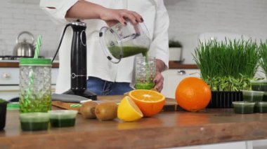 Genç kadın bir meyve ve sebze kokteyli dolduruyor. Yanında çim ve pipetle kavanoza.