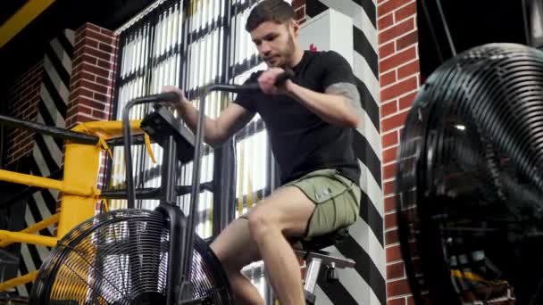 Young athletic male boxer trains on an exercise bike near the ring — Stock Video
