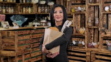 Elinde bir torba ekmek, sosis ve bakkaliye taşıyan genç bir kadın parmaklarıyla güzel bir işaret yapıyor..
