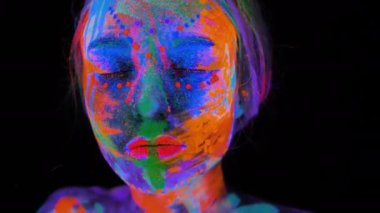 Neon ışıklı güzel bir genç kadın. Renkli makyajla mor ötesi ışıkta poz veren ve rujunu eliyle silen floresan makyajlı bir mankenin portresi.