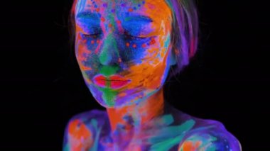 Neon ışıklı güzel bir genç kadın. Renkli makyaj ve meditasyon ile ultraviyole ışıkta poz veren floresan makyajlı bir model portresi