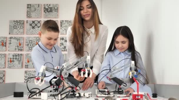 Junge schöne Mutter mit Sohn und Tochter spielen in der Robotikschule mit Robotern des Bauunternehmens — Stockvideo
