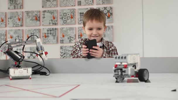 Liten pojke styr en robot med hjälp av sin telefon i en robotklass — Stockvideo