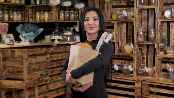 Μια νεαρή γυναίκα που κρατάει μια χάρτινη σακούλα με ψωμί, λουκάνικα και ψώνια κάνει μια πινακίδα εντάξει με τα δάχτυλά της, χαμογελώντας φιλικά.. — Αρχείο Βίντεο