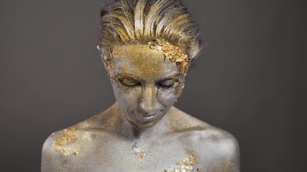 Bella giovane modella femminile con vernice oro e argento sulla pelle e sui capelli in studio — Video Stock