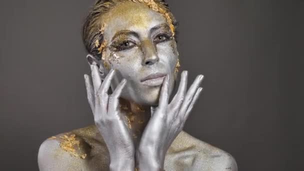 Hermosa joven modelo femenina con pintura dorada y plateada en su piel y cabello en el estudio — Vídeo de stock