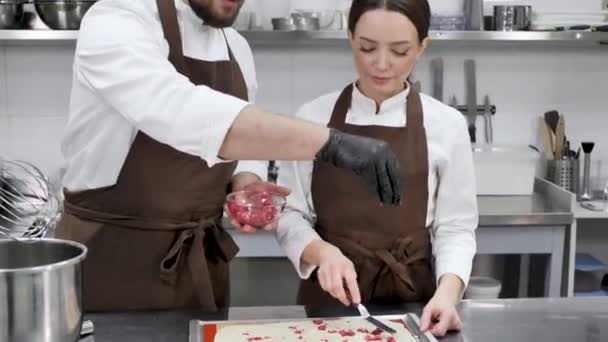 Paar banketbakkers, een man en een vrouw, koken in een professionele keuken en voegen bessen toe aan de cake. — Stockvideo