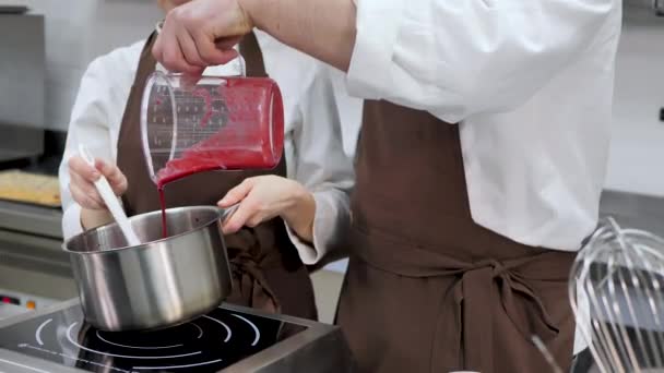 Man en een vrouw banketbakkers bereiden bessen kuli in een pot voor het vullen van de taart, mengen en toevoegen van suiker aan de siroop — Stockvideo