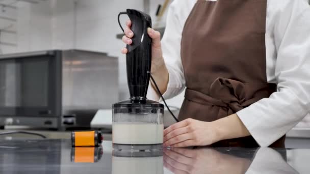 Chef de pastelaria feminina prepara um espelho de cobertura para um bolo, chicoteá-lo em um liquidificador e mede a temperatura — Vídeo de Stock