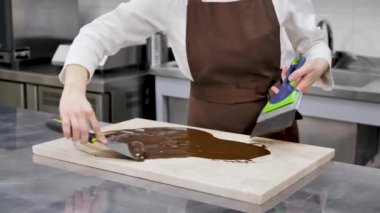 Dişi çikolatacı granit bir masada sertleştirilmiş çikolatayı karıştırmak için bir spatula kullanır..