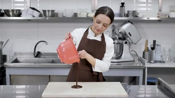 Vrouwelijke chocolatier giet gesmolten chocolade op een granieten tafel — Stockvideo