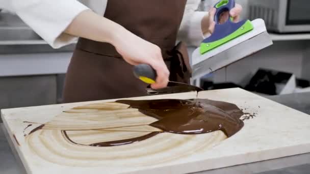 Female chocolatier uses a spatula to stir the tempered liquid chocolate on a granite table. — Stock Video