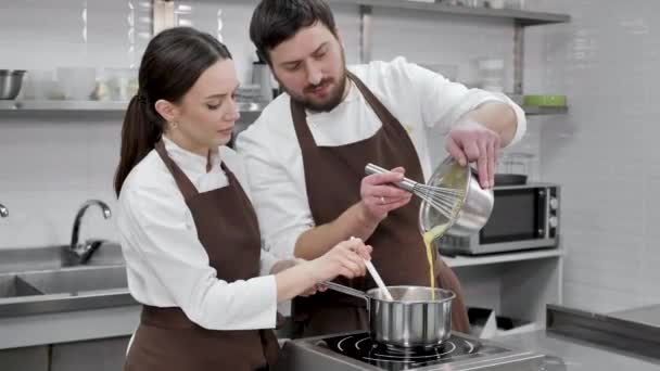 Bir çift şekerci, bir erkek ve bir kadın, profesyonel bir mutfakta bir krema hazırlar, krema için şekerlerin sarılarını tabana dökerler. — Stok video