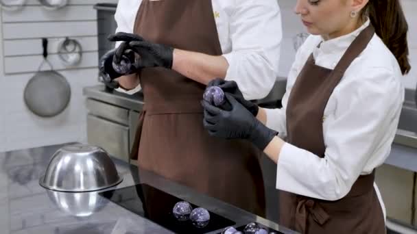 Två konditorer, en man och en kvinna, kopplar ihop chokladhemisfärerna och smälter dem på en varm skål. — Stockvideo